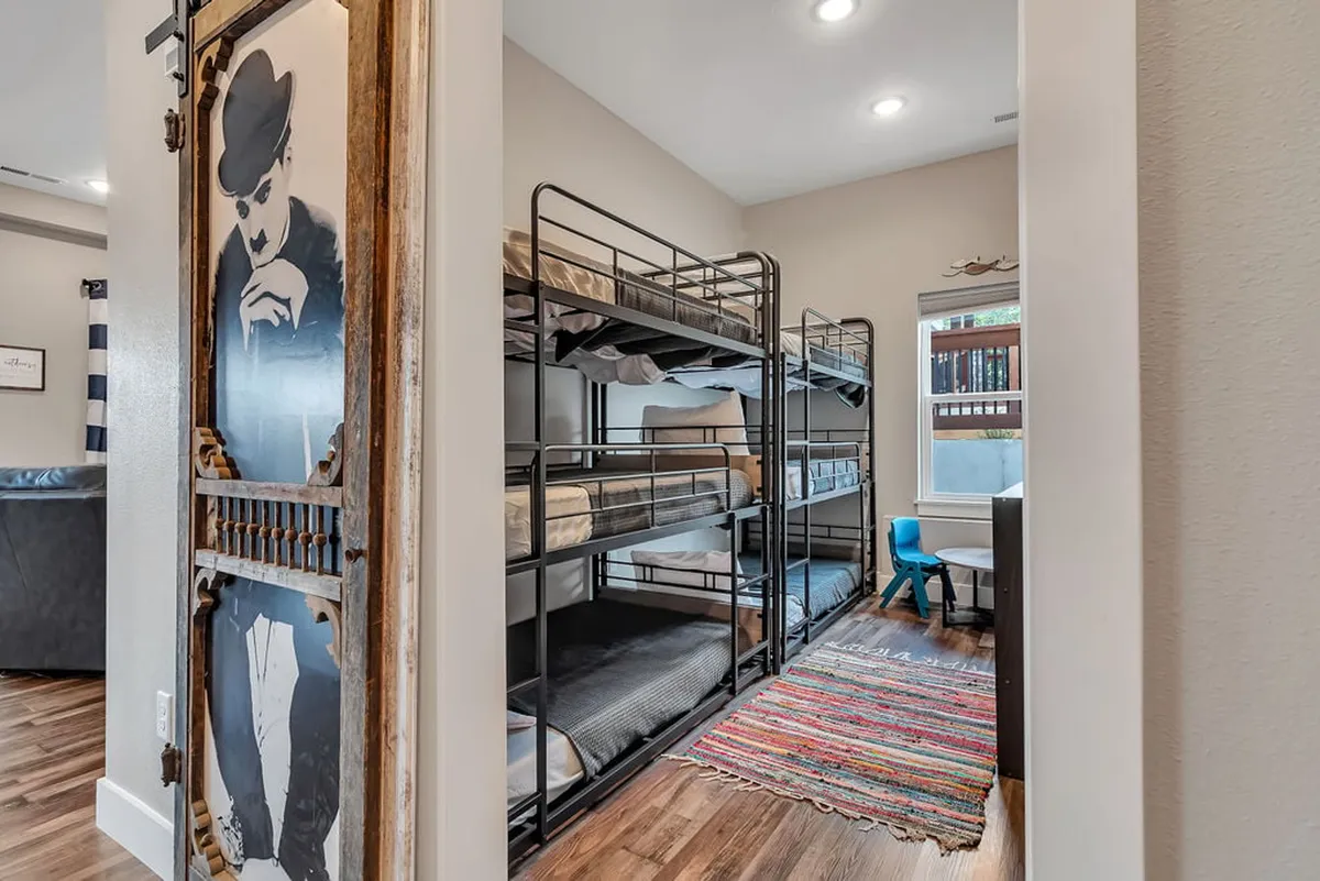A bright and playful bunk room featuring built-in bunk beds, a colorful rug, and a decorative door. The space is designed for kids or cousins' sleepovers, encouraging both play and restful nights.