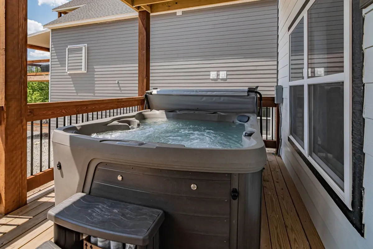 An outdoor deck area featuring a hot tub surrounded by lush greenery, offering a tranquil spot for relaxing in nature. The scene exudes privacy and comfort, ideal for unwinding after an energetic game night or a day full of activities.