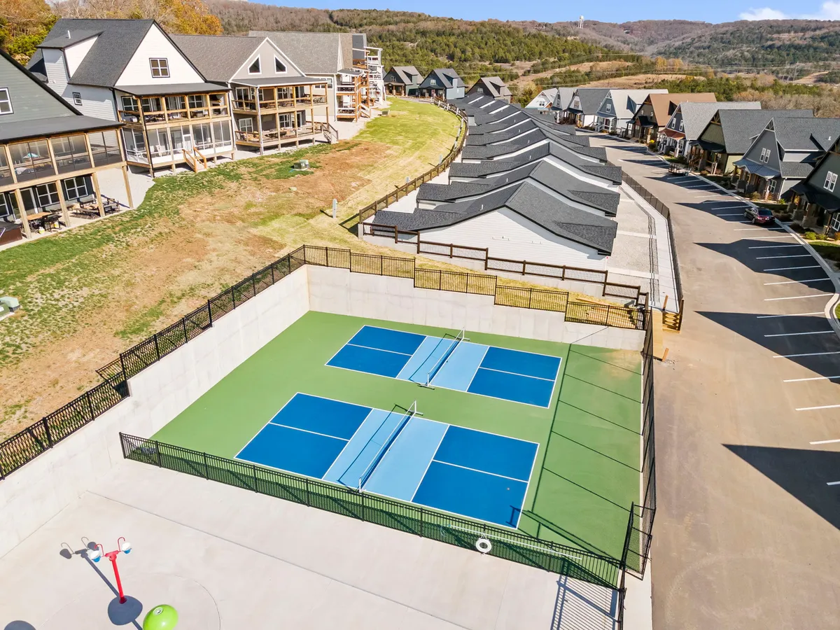 A vibrant view of outdoor tennis and pickleball courts with residential buildings and landscaped hills in the background. The open, paved walkways show step-free access, inviting guests of all abilities to join games or spectate.