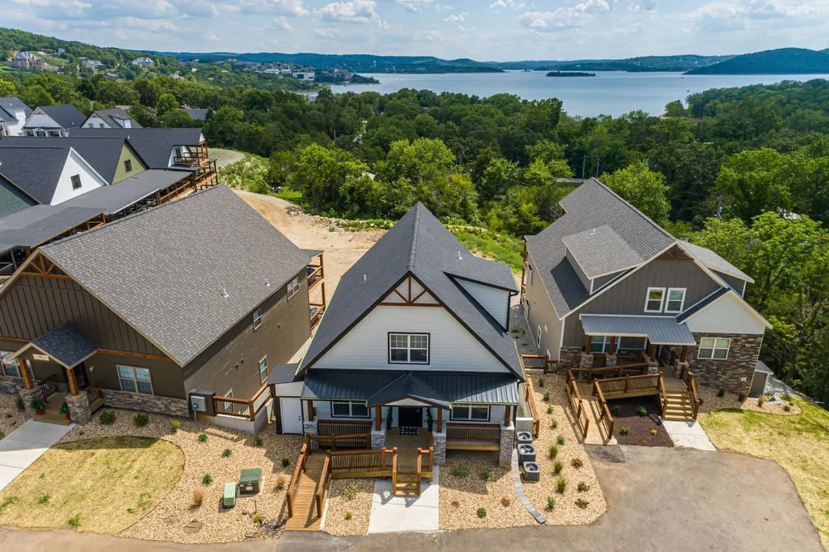 A broader exterior perspective showing three distinct houses surrounded by lush greenery and overlooking a lake. The setting radiates serenity and togetherness, suggesting a multi-generational retreat with room for everyone.
