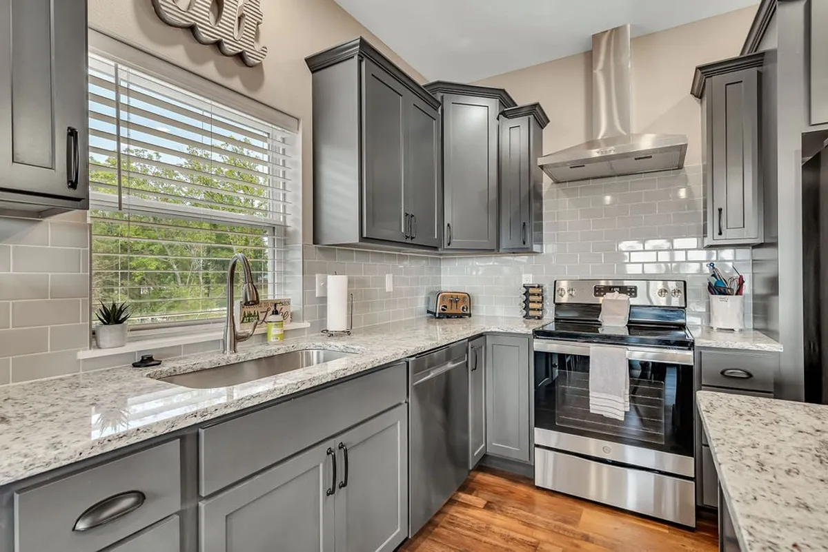 This image features a modern, open kitchen with sleek granite countertops, stainless steel appliances, and plenty of natural light streaming through a window. The space is designed for both cooking and entertaining, with ample workspace and a welcoming atmosphere for family meal prep or baking sessions.