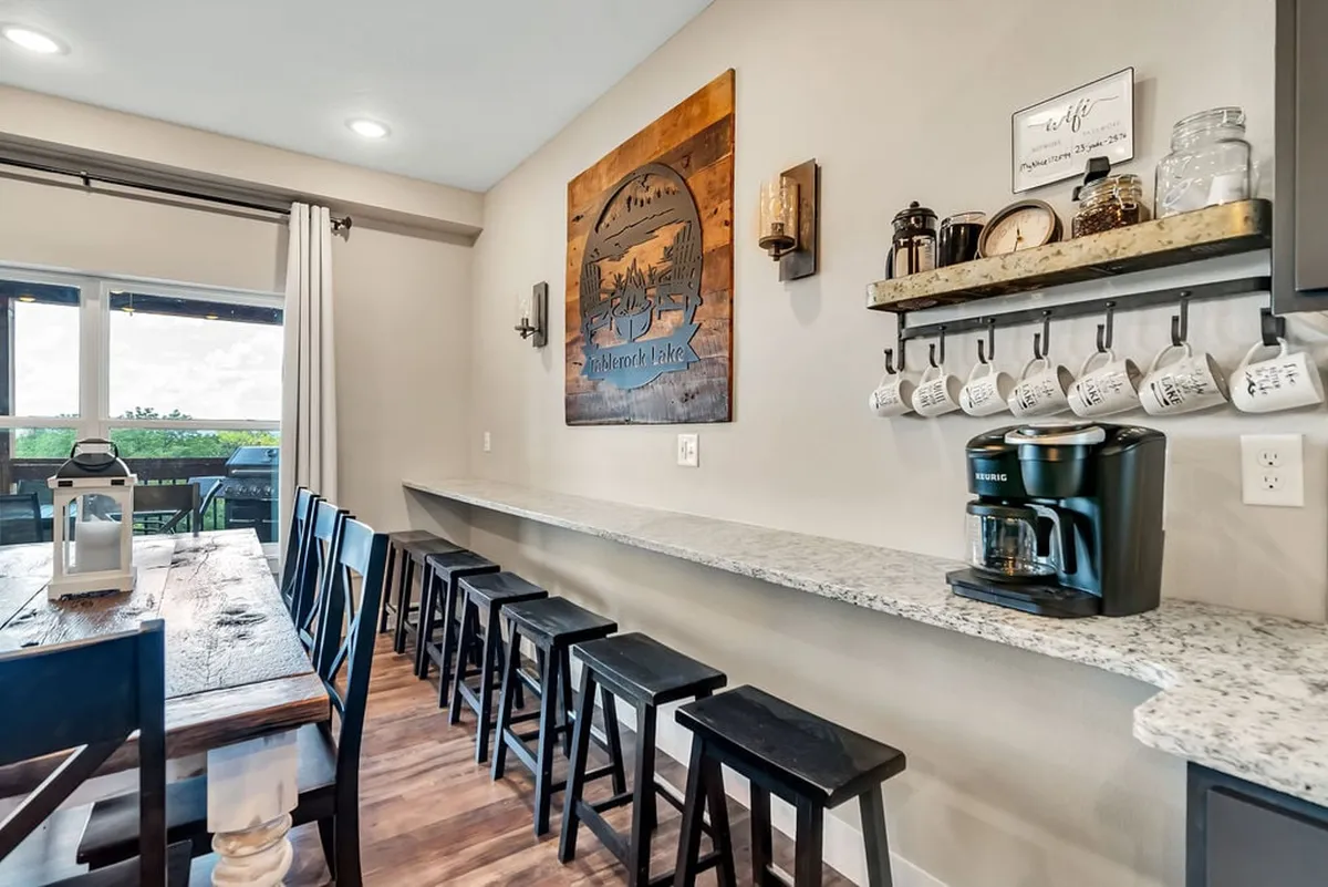 A cozy dining nook with a granite countertop, wooden dining table, coffee maker, and rustic wall art. The scene is warm and inviting, perfect for quiet morning rituals or intimate family breakfasts.