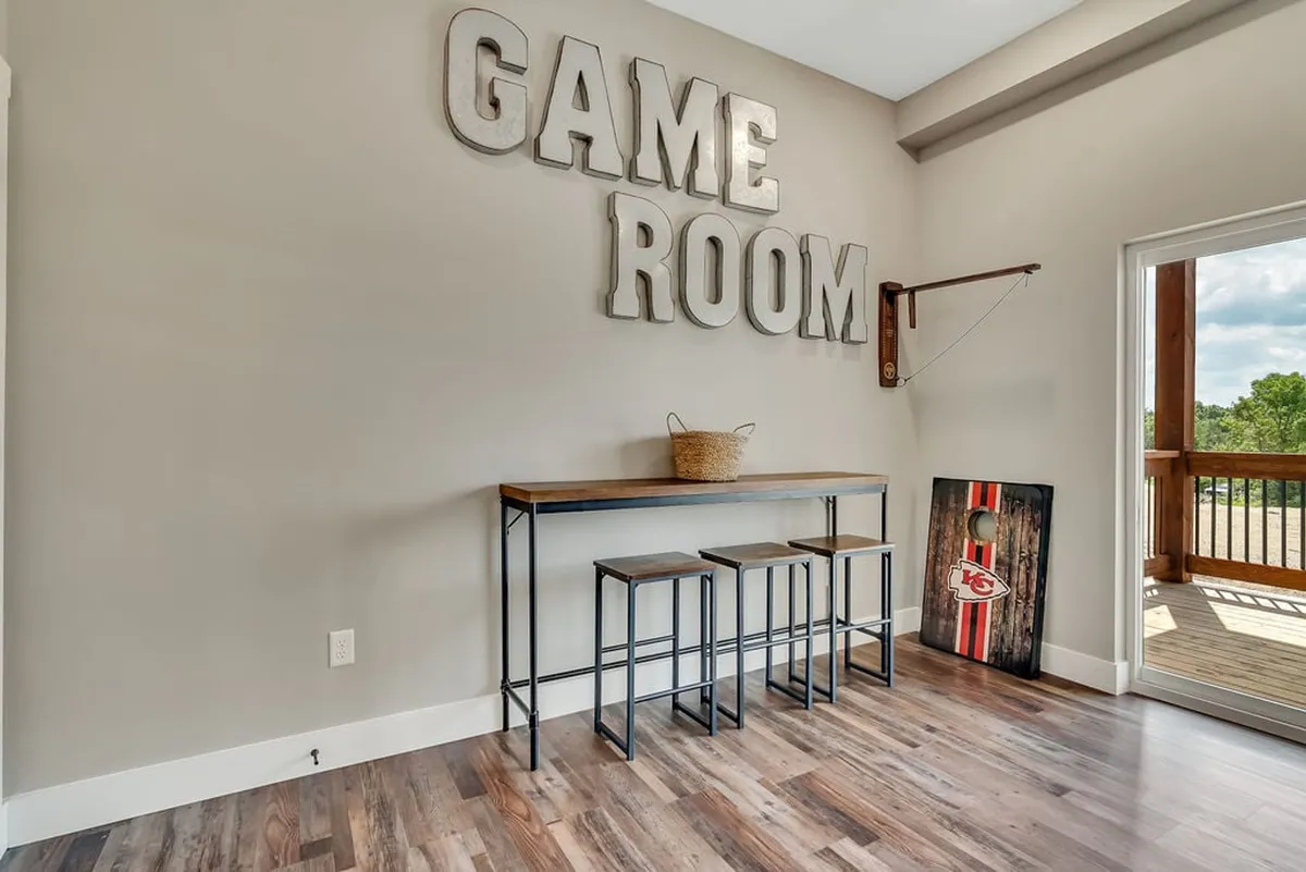 This interior image features a large 'GAME ROOM' sign above a bar table with stools and a visible cornhole board, highlighting a dedicated, playful atmosphere for social gatherings and various games.