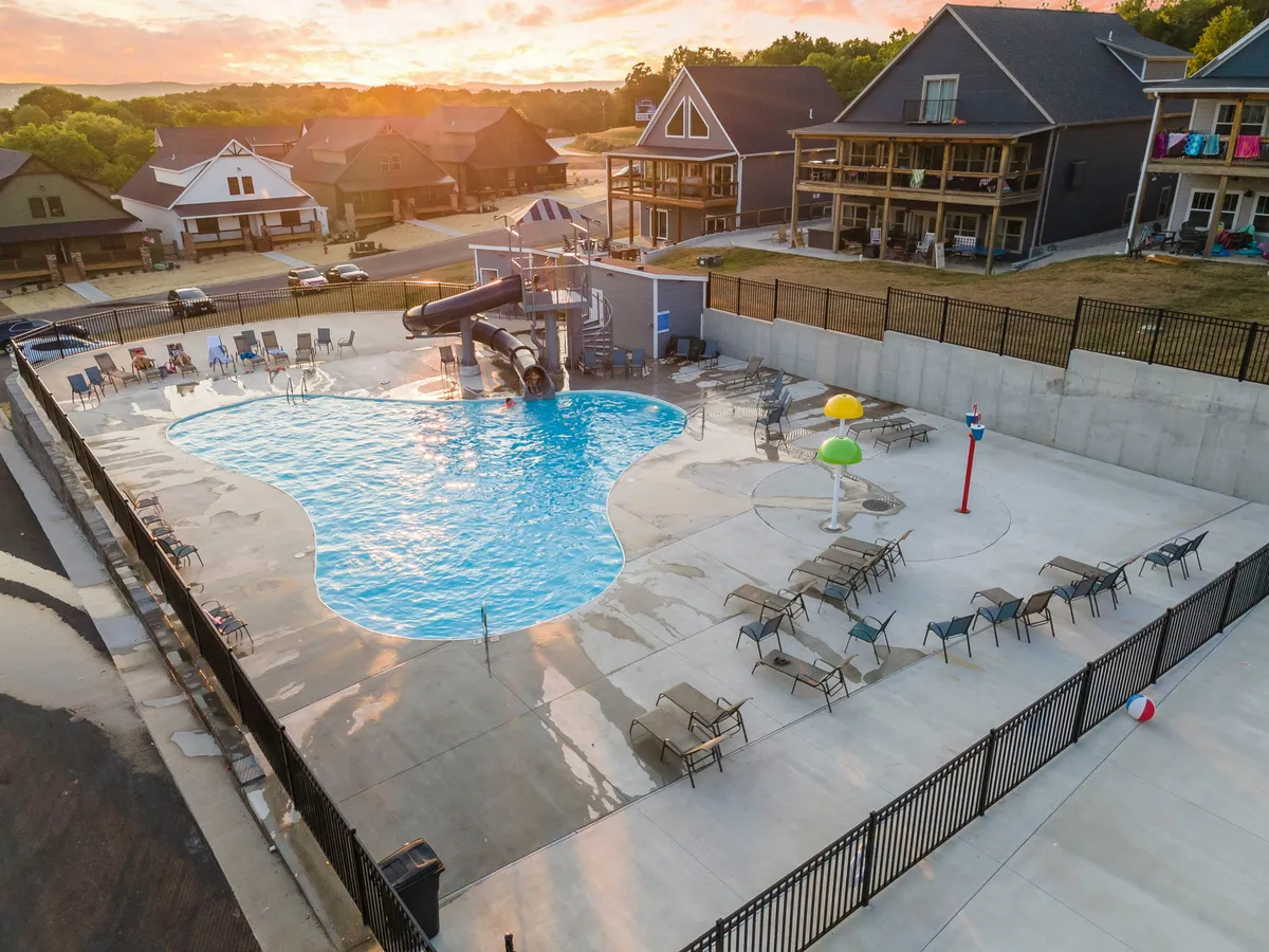 A lively outdoor resort pool area with a water slide, colorful water features, and lounge chairs, set in a bright, social environment. Children are seen playing, and the atmosphere is energetic and family-friendly, embodying the spirit of resort amenities.