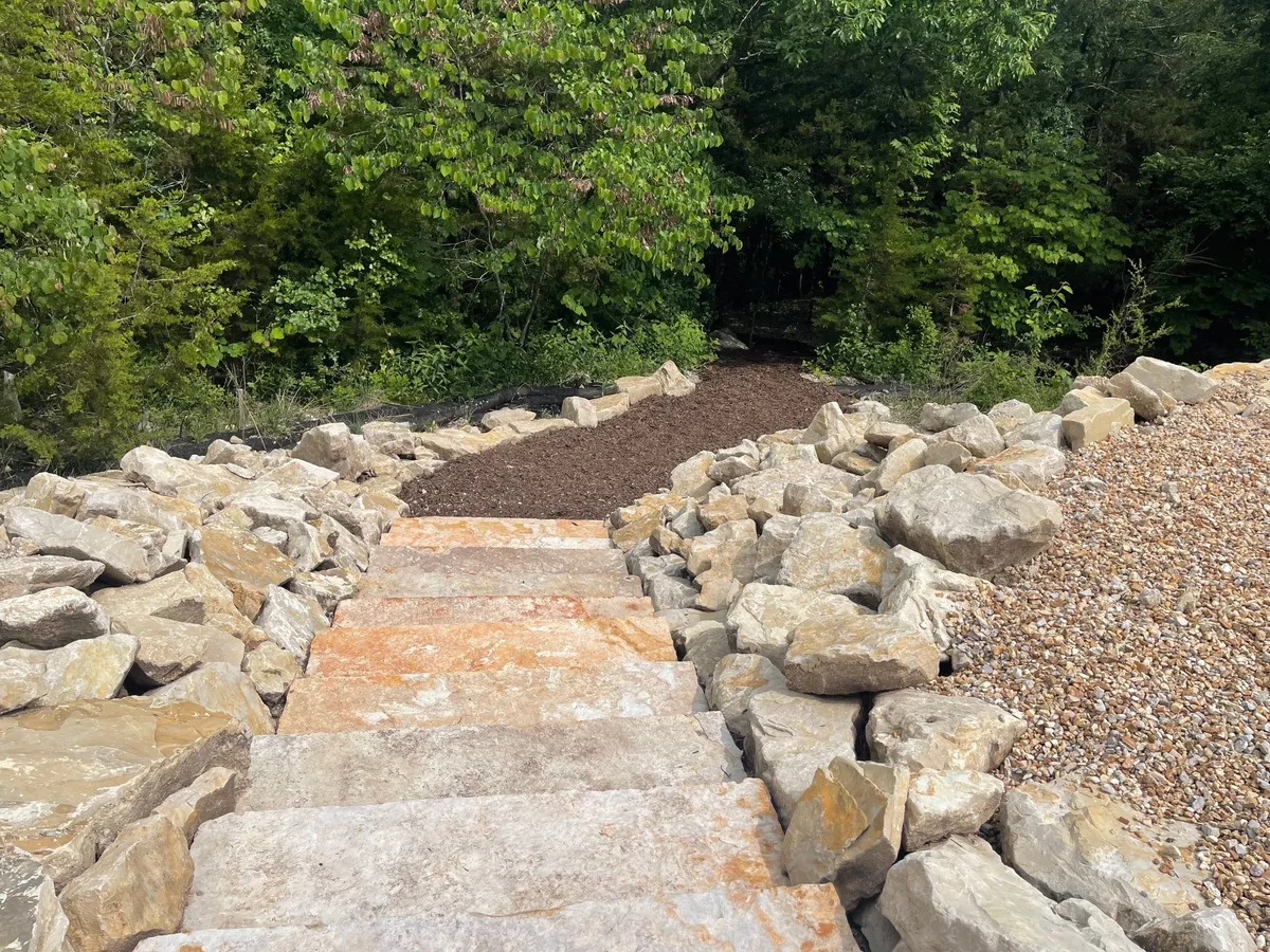 A peaceful gravel pathway bordered by stone steps and surrounded by rich greenery. The path winds gently through a natural landscape, inviting guests to stroll, explore, and unwind amidst the outdoors.