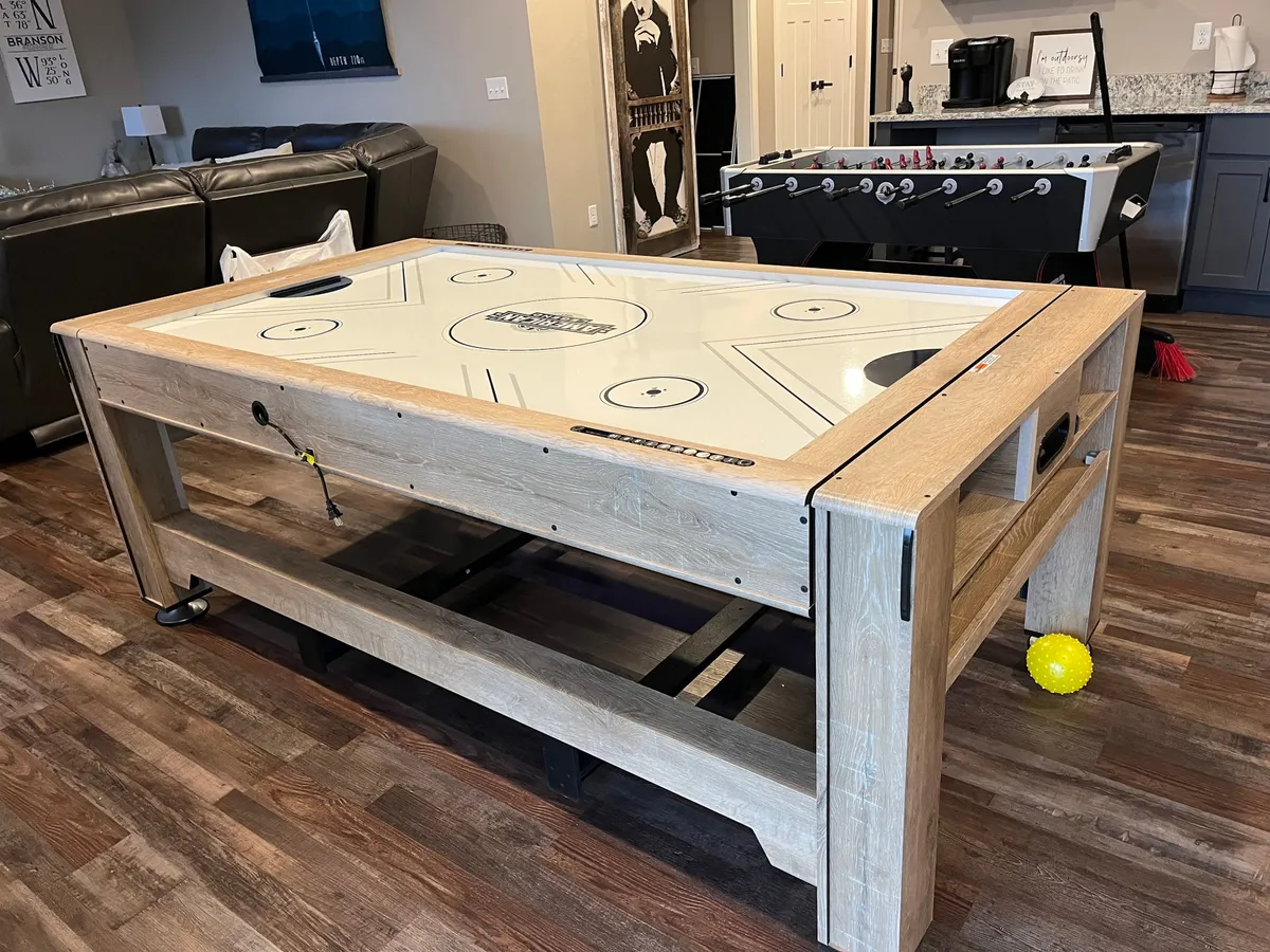 This scene showcases an air hockey table and foosball table set up next to a comfortable sofa seating area. The space is designed for interactive play and group enjoyment, embodying the lively, fun-focused spirit described in the section.