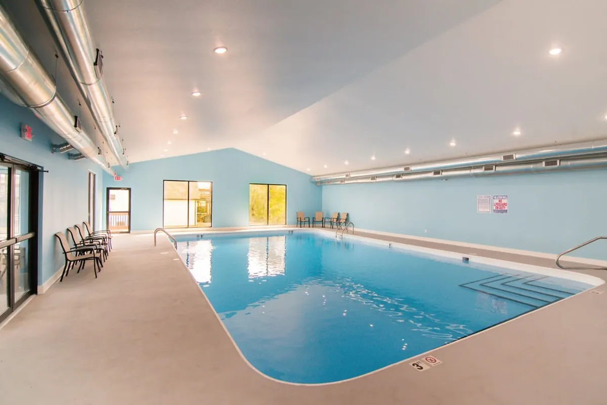 This interior scene showcases a modern indoor swimming pool filled with natural light from large windows. Comfortable seating and a relaxed ambiance make it clear this space is perfect for year-round swimming, even during cooler weather or rainy days.