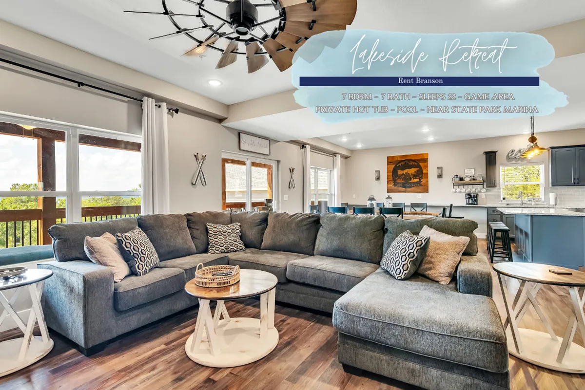 A comfortable, inviting living room featuring a large sectional sofa, round coffee table, decorative pillows, wooden ceiling fan, and an open kitchen area. The space exudes warmth, perfect for gatherings and relaxing with family or friends. The overall mood is cozy and welcoming, ideal for both socializing and unwinding.
