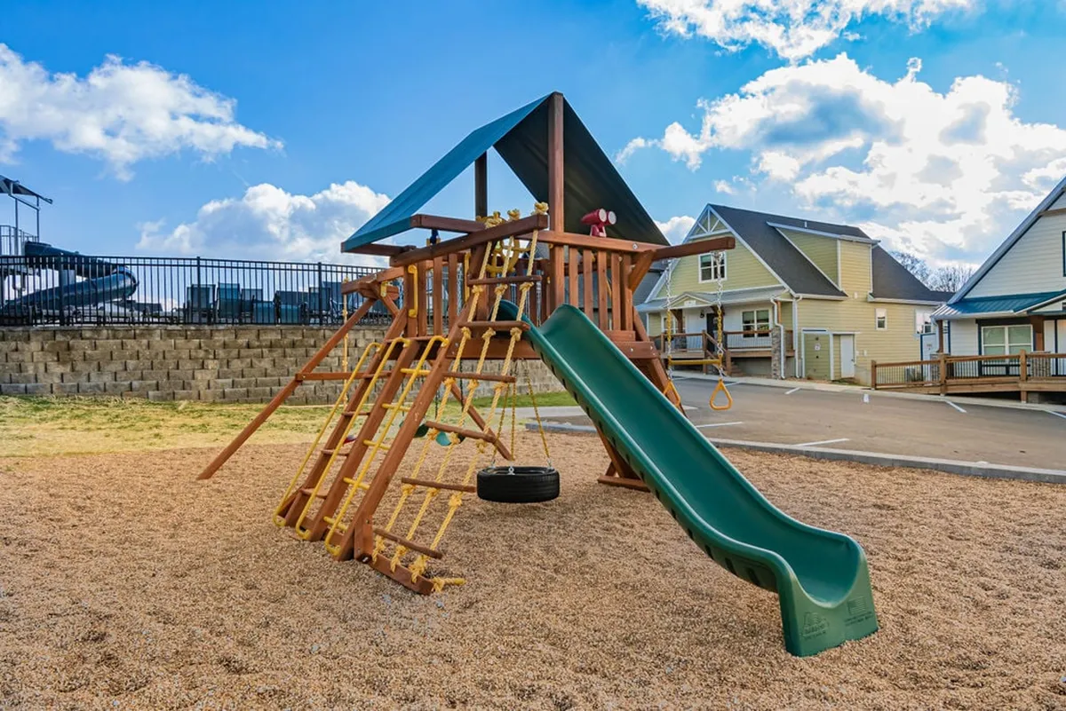 A joyful playground scene with a playground structure, slide, swing set, and sandbox, surrounded by green open spaces. Children play while adults supervise, highlighting the family-friendly and inclusive environment.