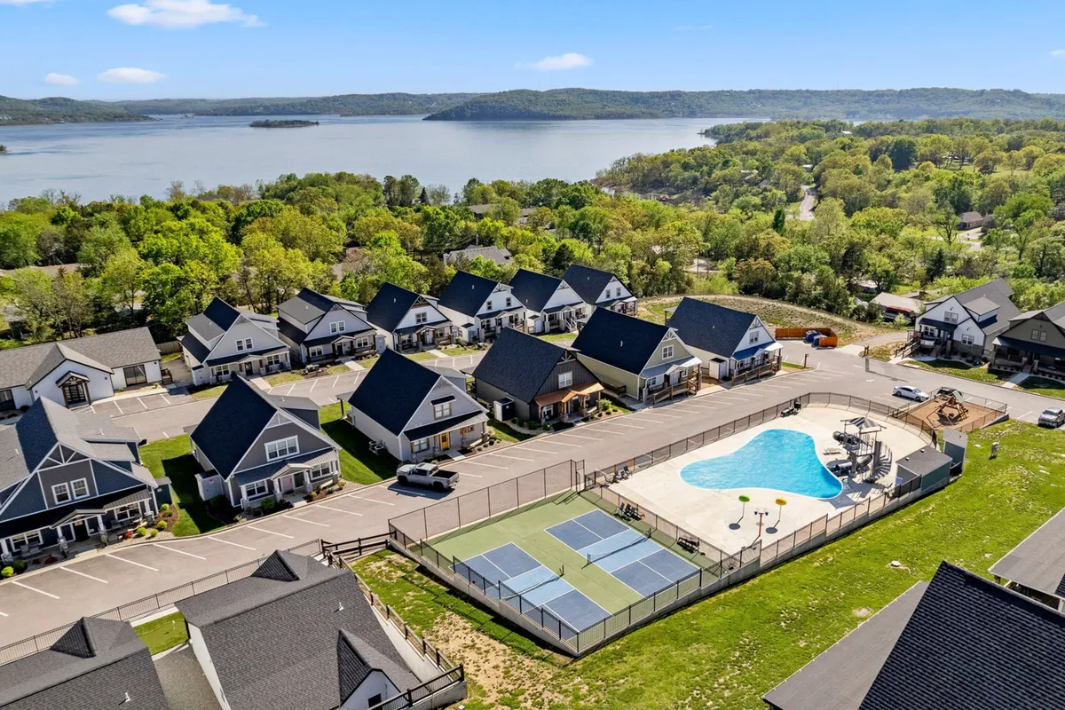 An exterior view of the community amenities, including a swimming pool, tennis courts, and a scenic lake backdrop. The image captures a broader sense of the recreational options and resort-style environment available at Branson Cove.