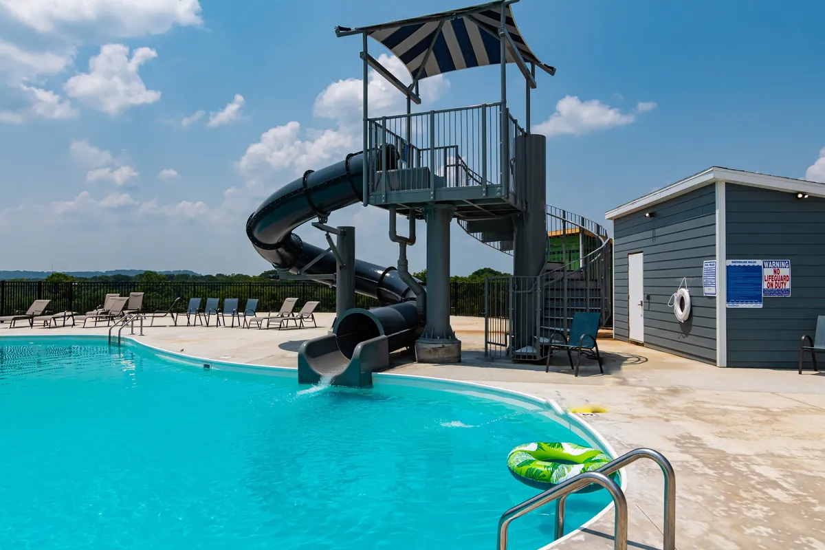 A playful and energetic scene of an outdoor swimming pool with a water slide, lounge chairs, and a lifeguard station. The area is lively, suggesting memorable summer days full of fun and socializing.