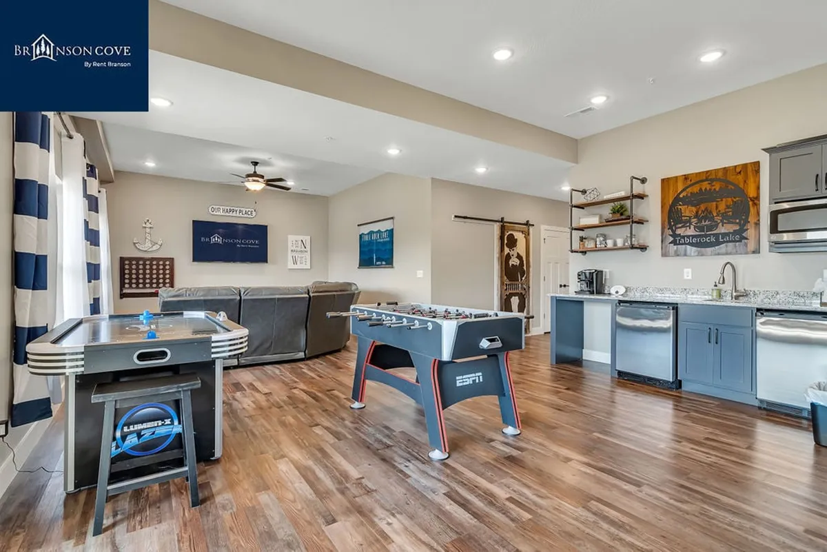 A vibrant game room featuring a foosball table and an air hockey table, complemented by a comfortable sofa and a kitchenette area with a wet bar. The space is well-lit and designed for group activities, offering a fun and inviting setting for socializing and friendly competition.